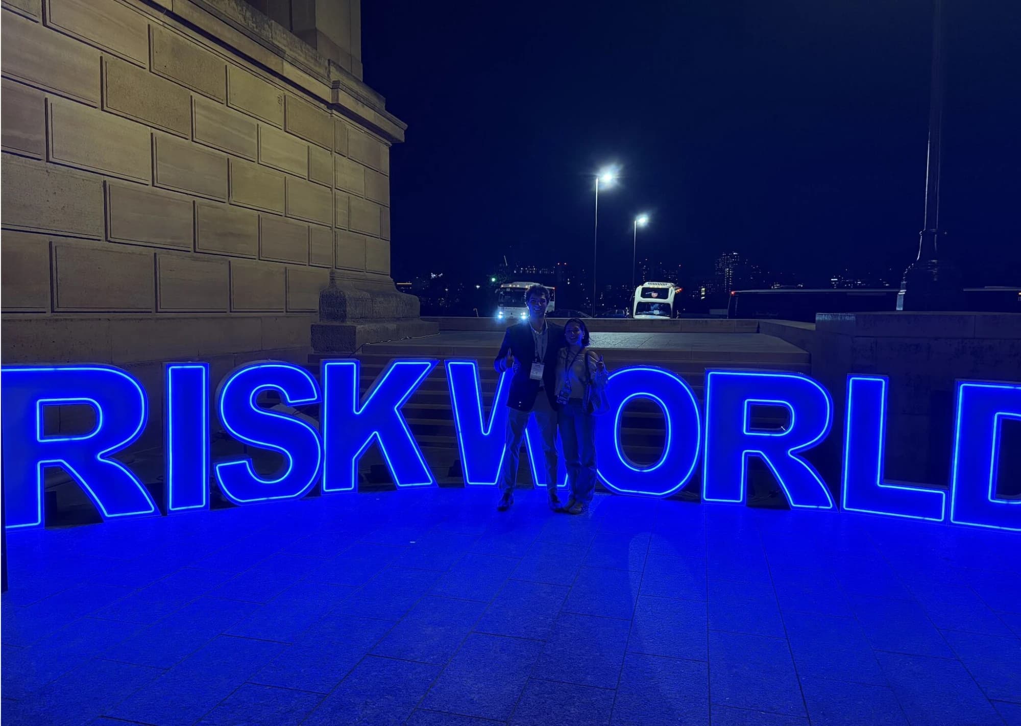 Naomi and a fellow student at the lit-up RISKWORLD sign at night